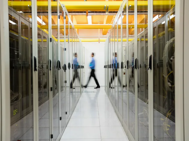 Aisle between glass-fronted server racks in a data center, with a person walking through in motion blur