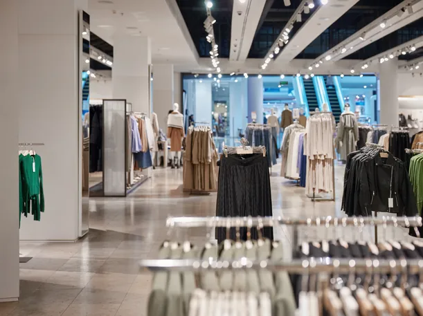 Fashion store interior with clothing rails, mannequins, track lighting and escalators in the background