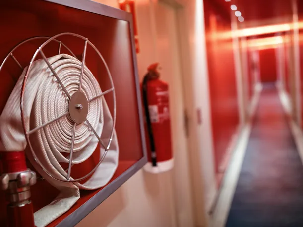 Fire hose reel and extinguisher in a red wall cabinet beside a building corridor